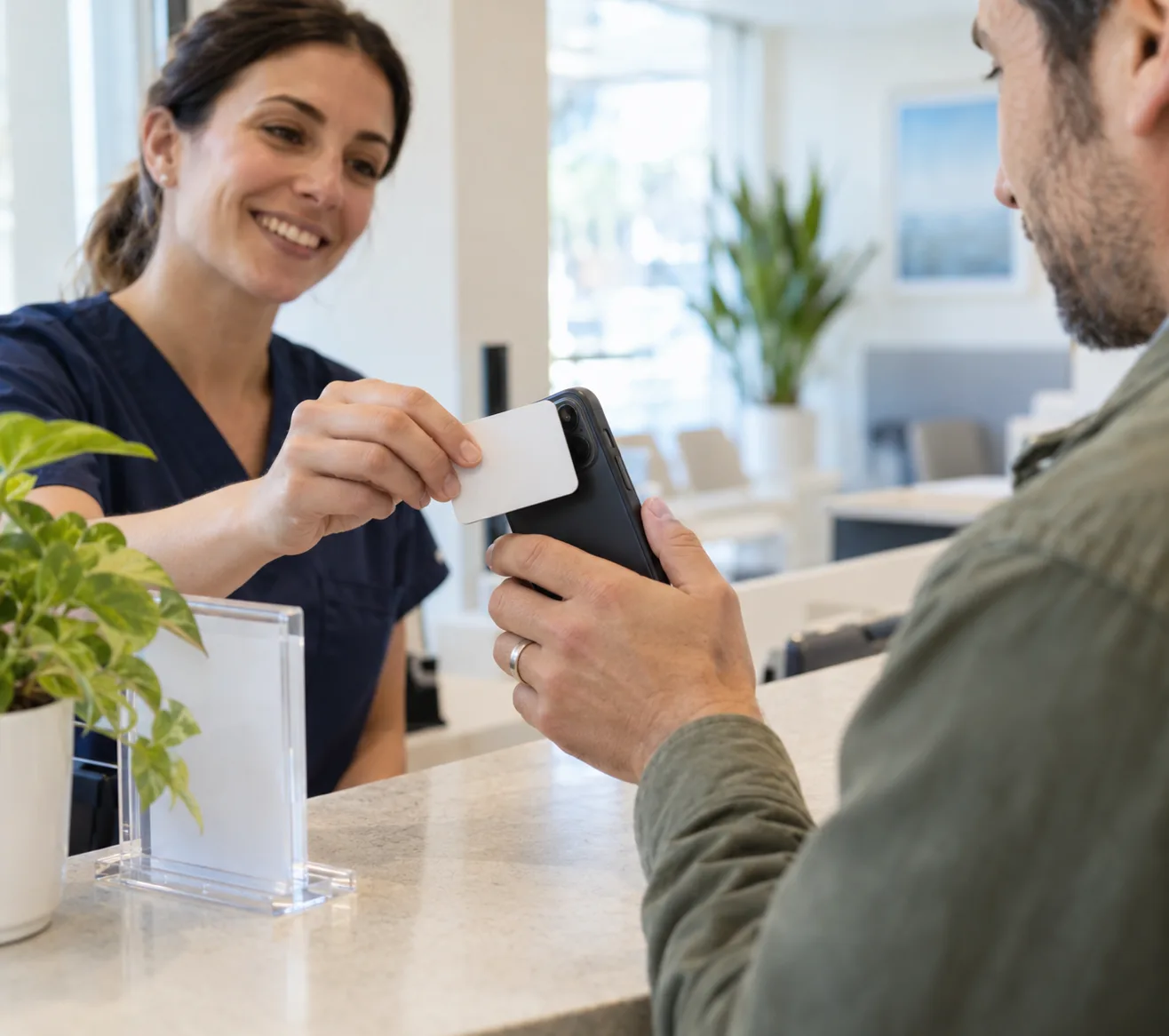 Una card NFC avvicinata a uno smartphone al bancone di una reception, accanto a un espositore in plexiglass