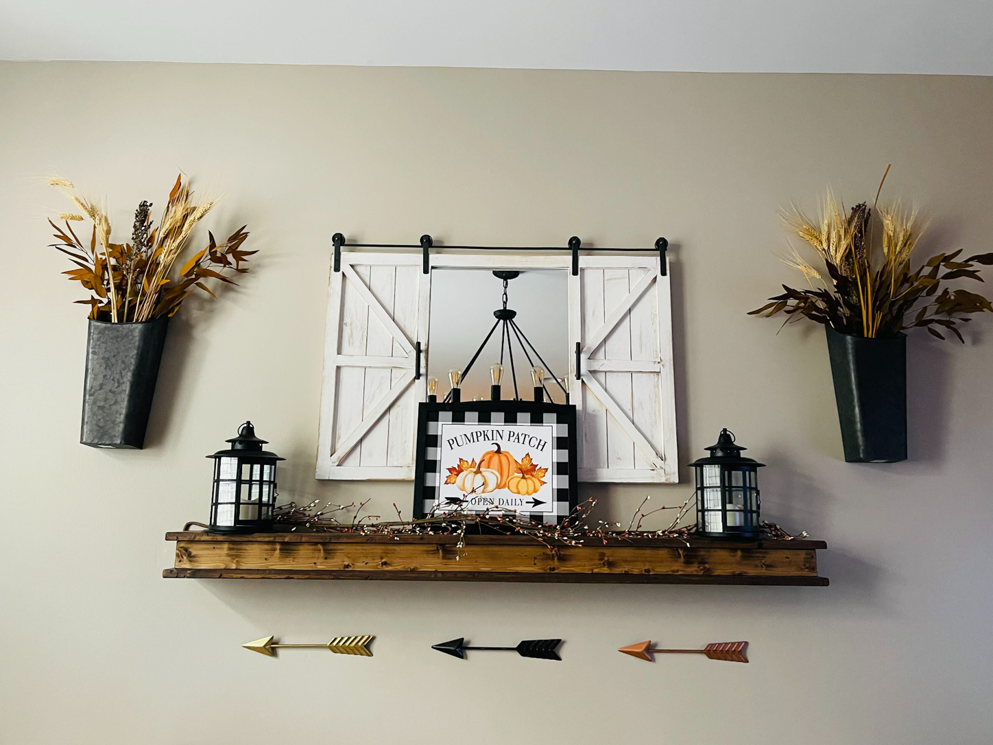 Floating wood shelf mounted on a wall with framed art and lanterns arranged on it