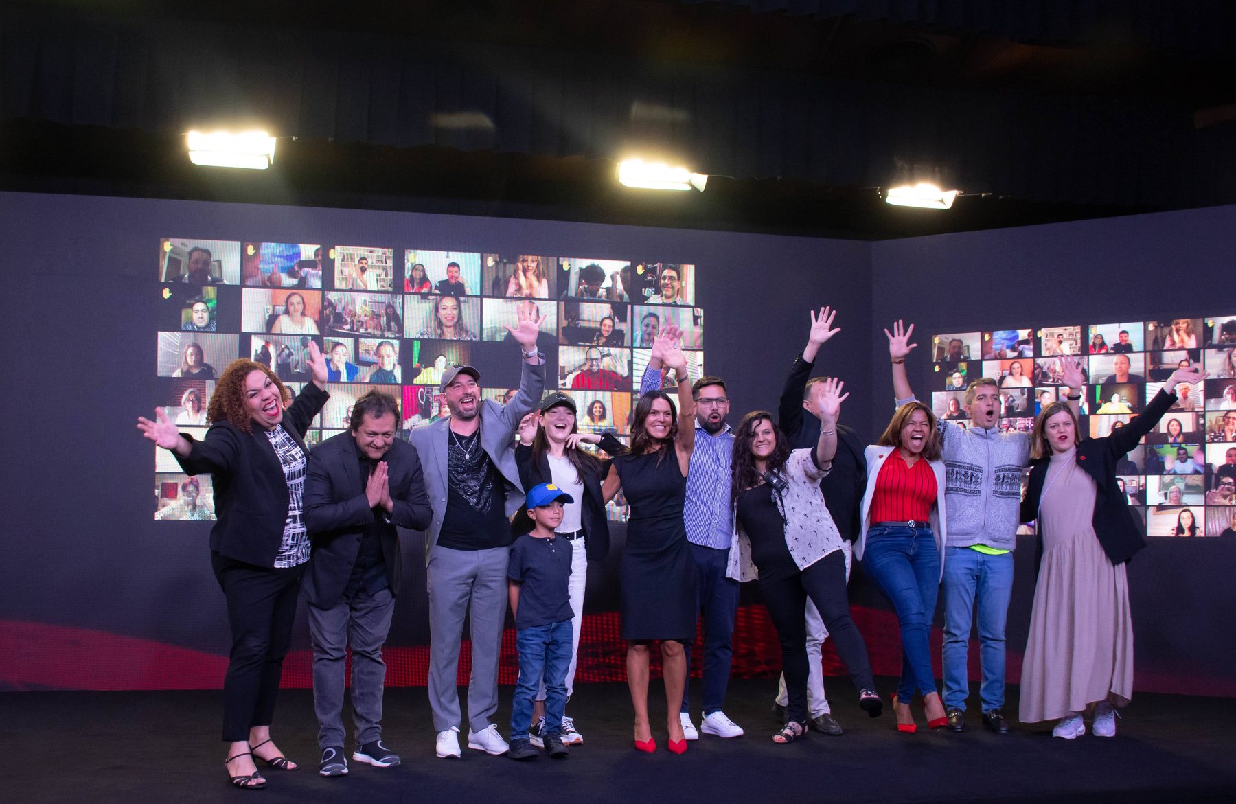 Grupo celebrando en el escenario junto a la pantalla de videollamadas de asistentes remotos, en una edición anterior de la Cumbre.