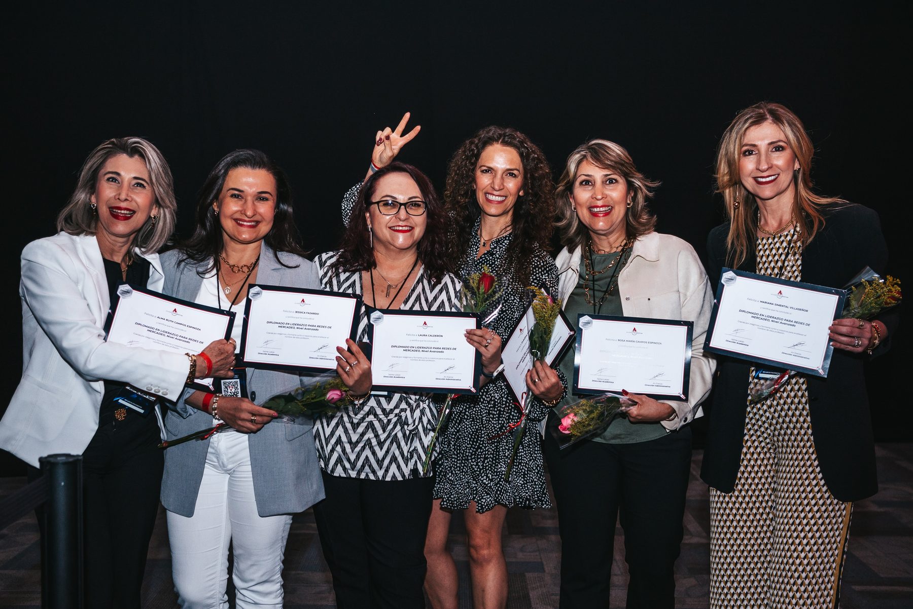 Seis asistentes en el escenario recibiendo su diploma de liderazgo y un ramo de flores.