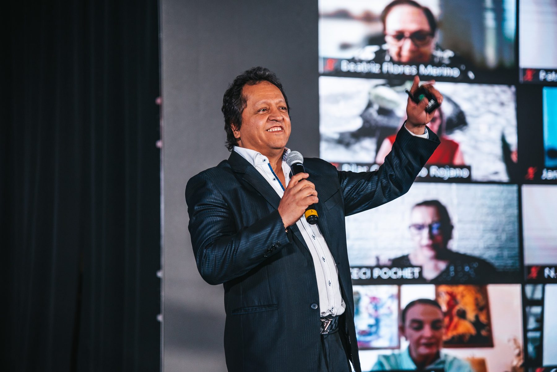 Juan Carlos Barrios con micrófono en el escenario de la Cumbre, con la pantalla al fondo.