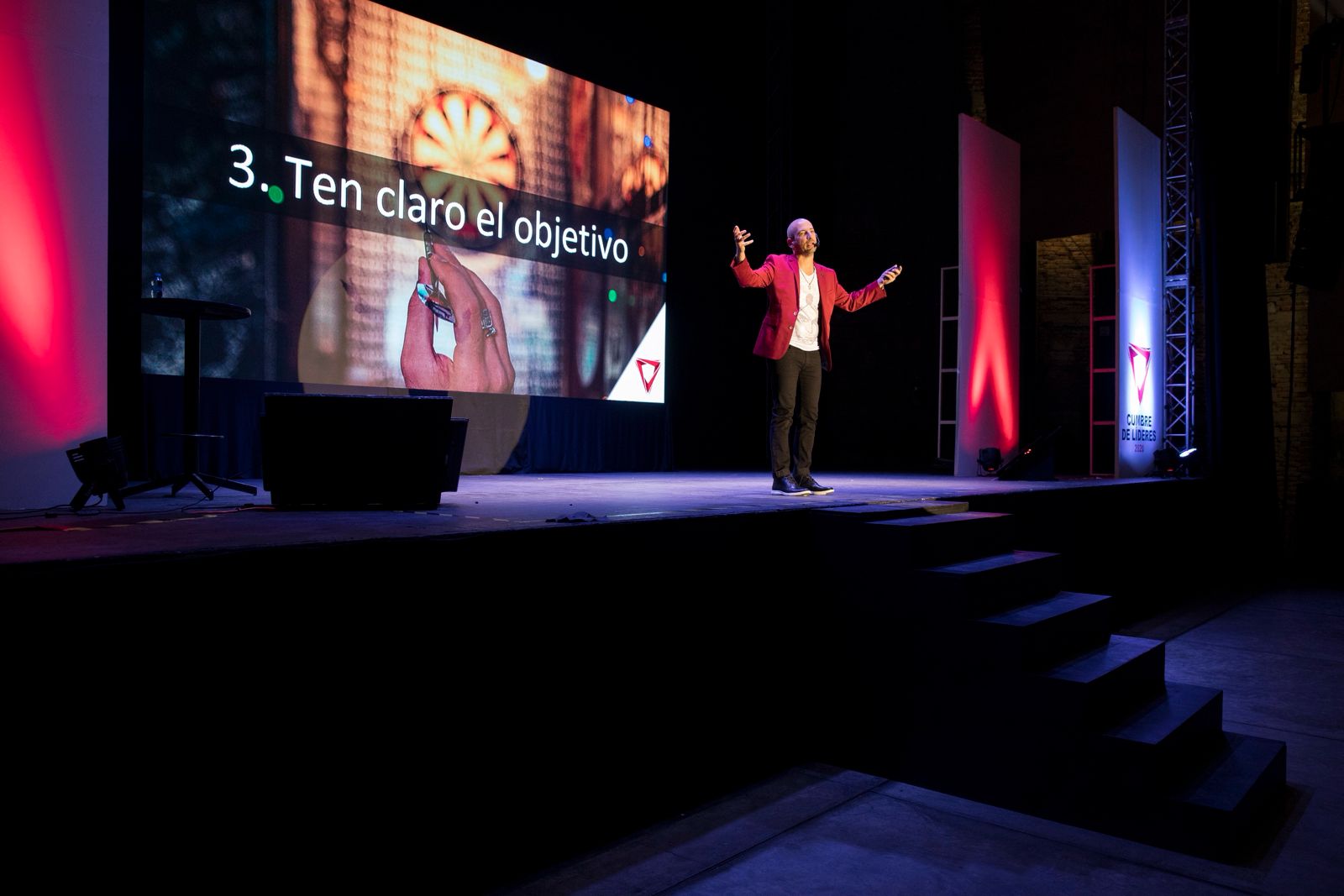 Jaime Lokier en el escenario con los brazos abiertos, frente a una diapositiva de su charla.