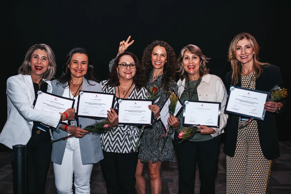 Seis asistentes en el escenario recibiendo su diploma de liderazgo y un ramo de flores.