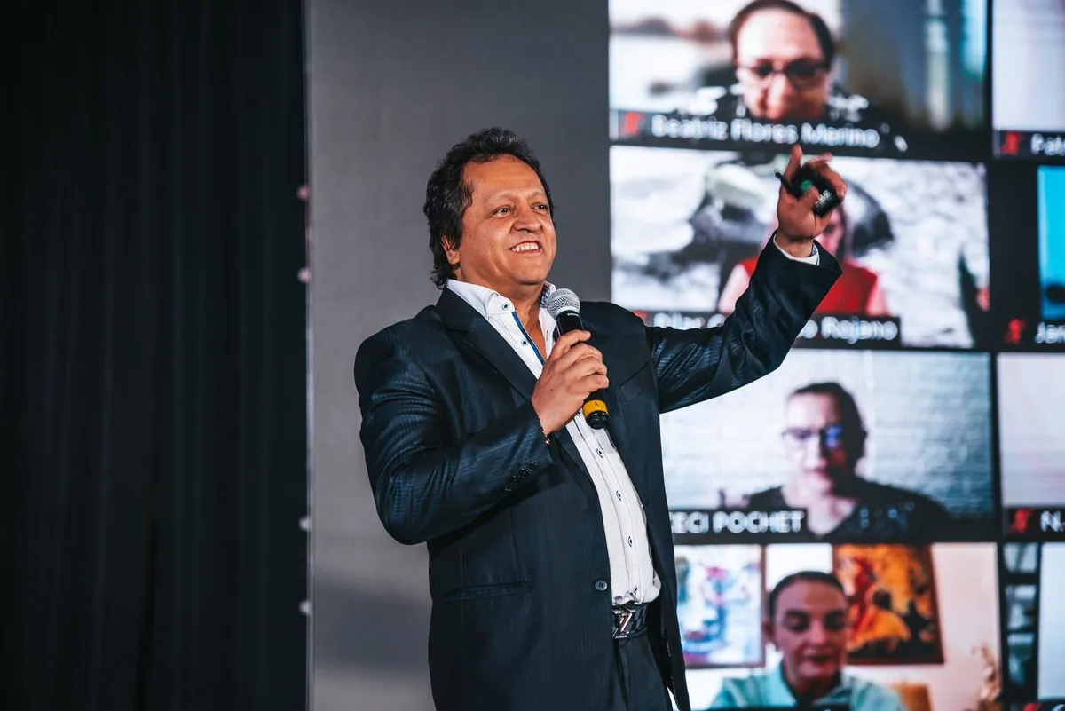Juan Carlos Barrios con micrófono en el escenario de la Cumbre, con la pantalla al fondo.