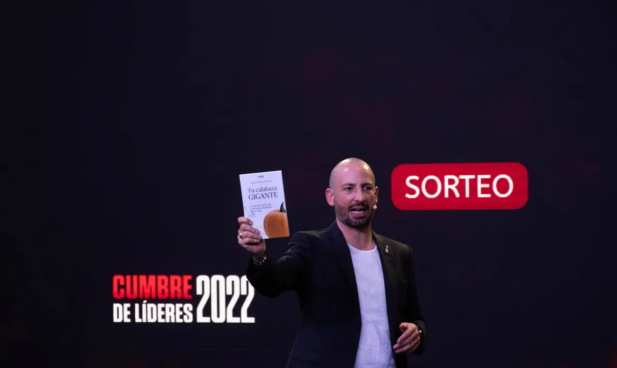 Jaime Lokier en el escenario, con micrófono de diadema, mostrando un libro durante el sorteo.