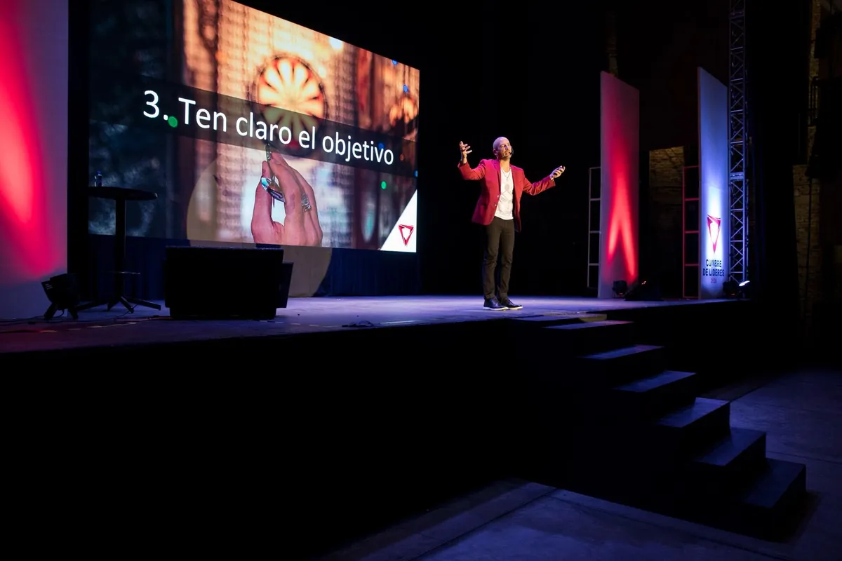 Jaime Lokier en el escenario con los brazos abiertos, frente a una diapositiva de su charla.