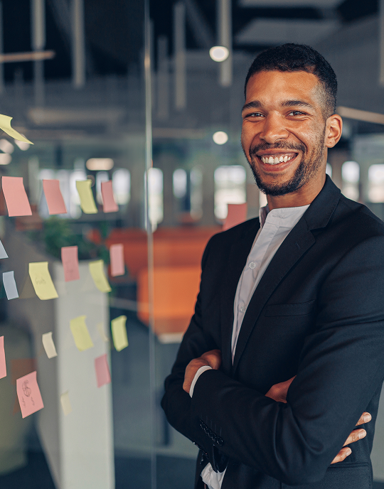 Smiling professional standing beside a glass wall covered in sticky notes