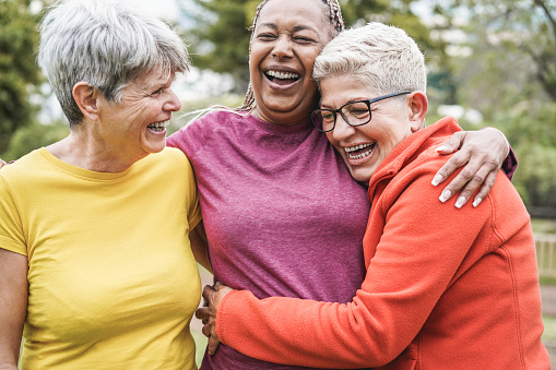 Three women laughing together outdoors with their arms around each other.