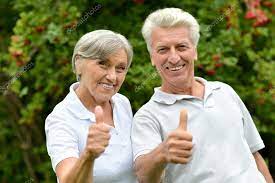 A couple smiling and giving a thumbs up in a garden.