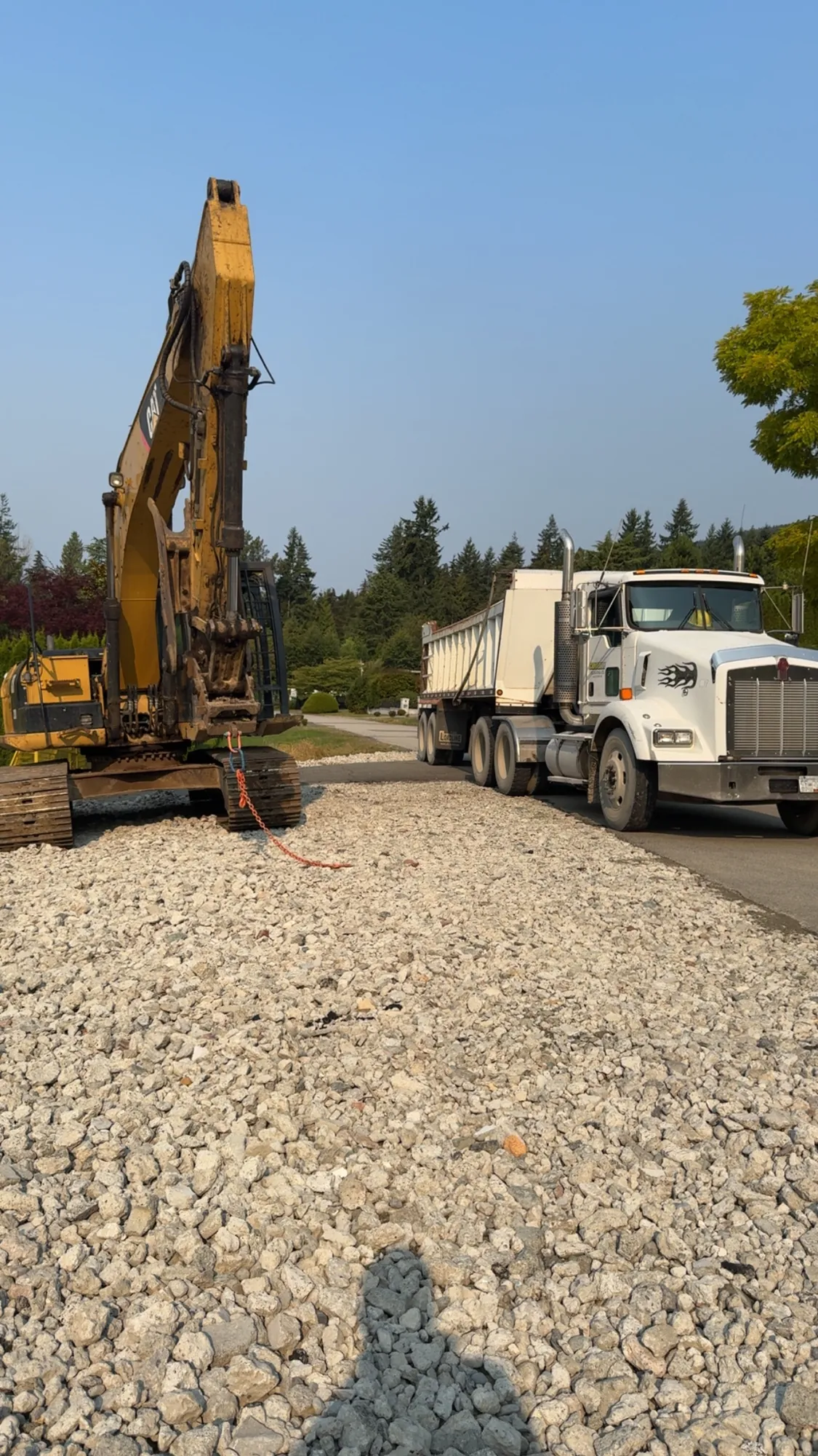 Dump truck and slinger spreading gravel fill on a construction site in Vancouver