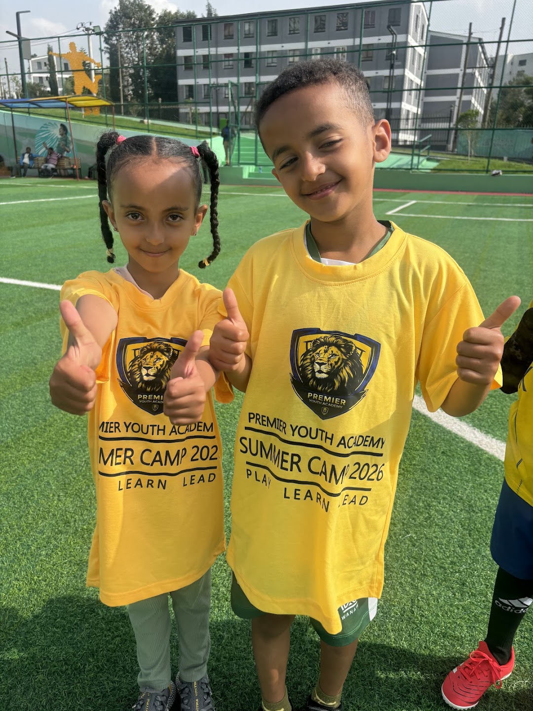 Two smiling PYA players giving a thumbs-up on the football pitch