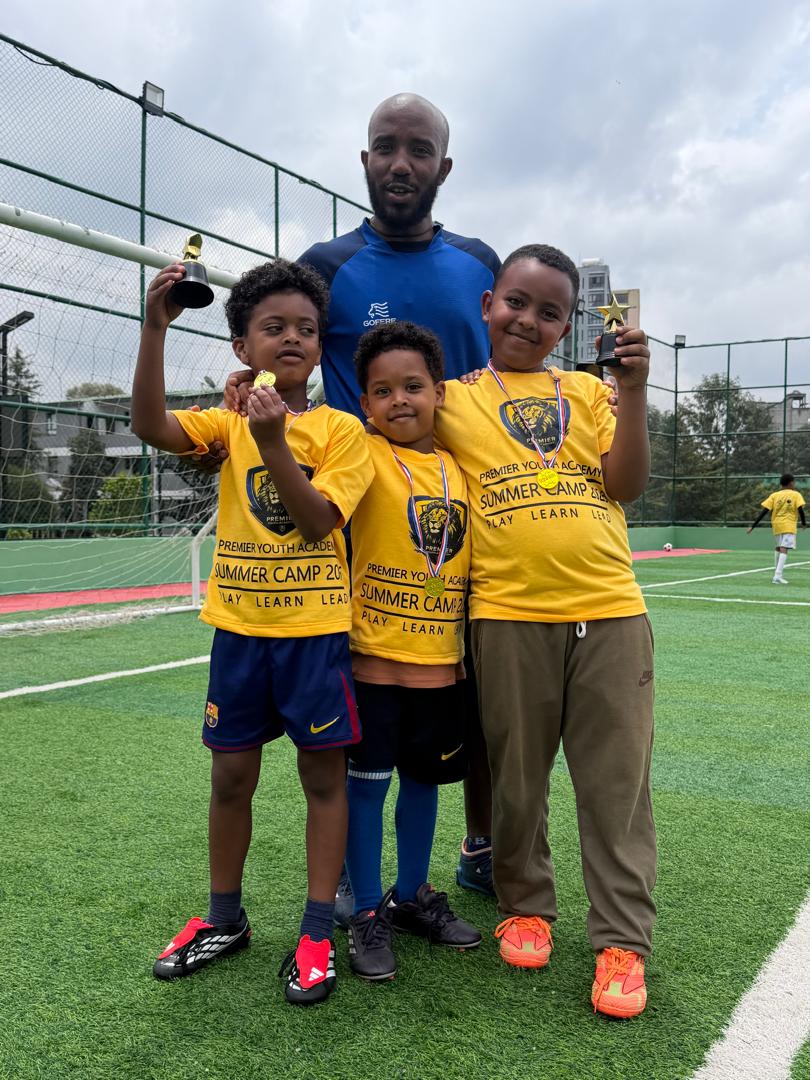 A PYA coach with three young players celebrating with medals and trophies
