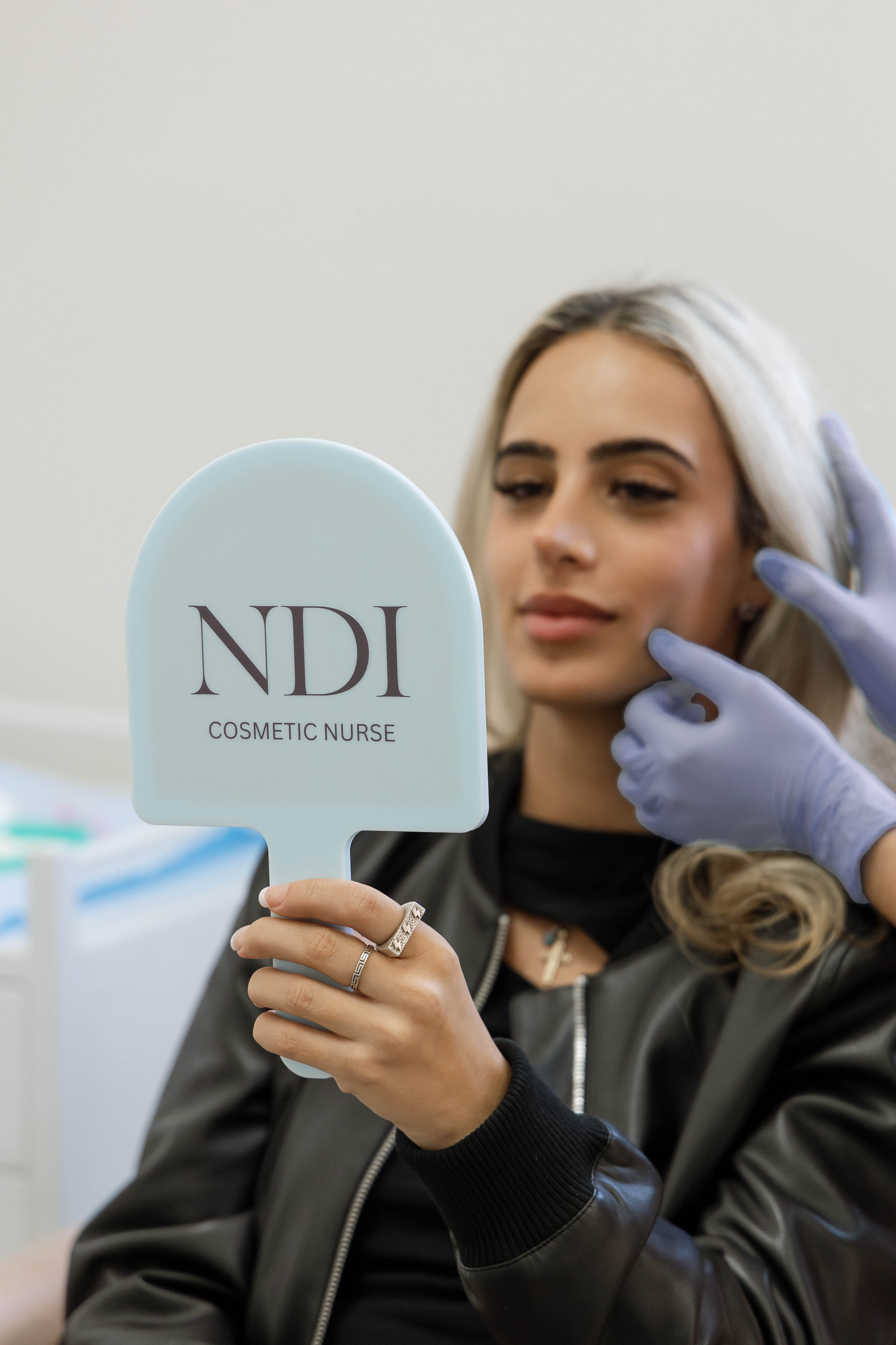 A client holding an NDI Cosmetic Nurse branded hand mirror in clinic