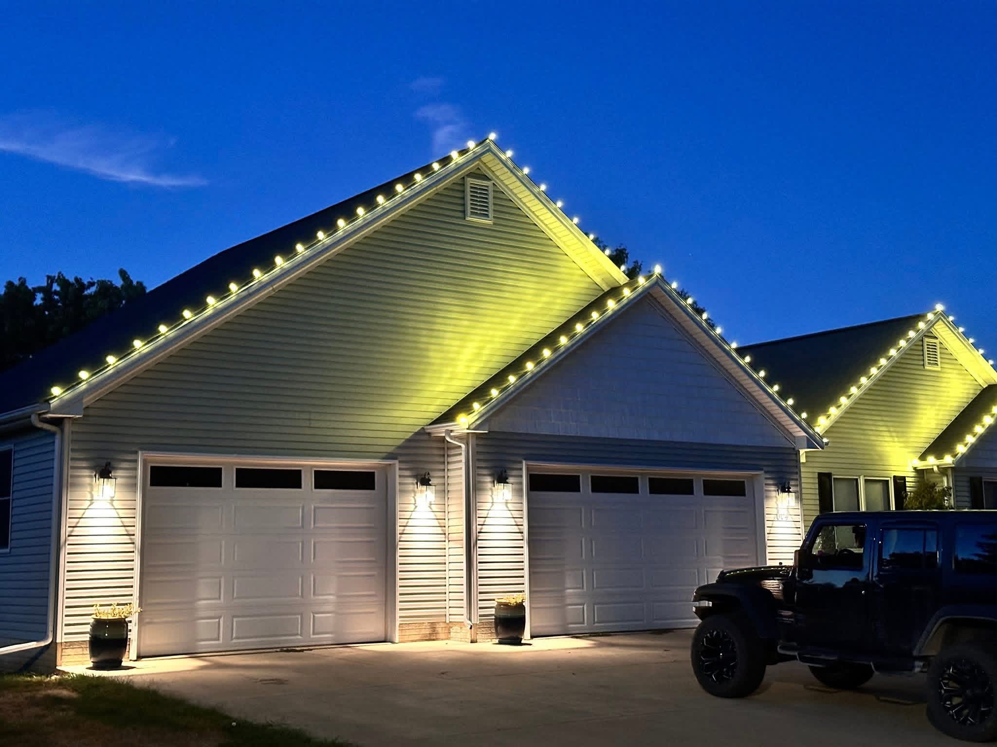 Custom holiday Christmas lighting installed along a home roofline at night