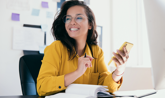Happy woman with a mobile phone in one hand and a pen in the other