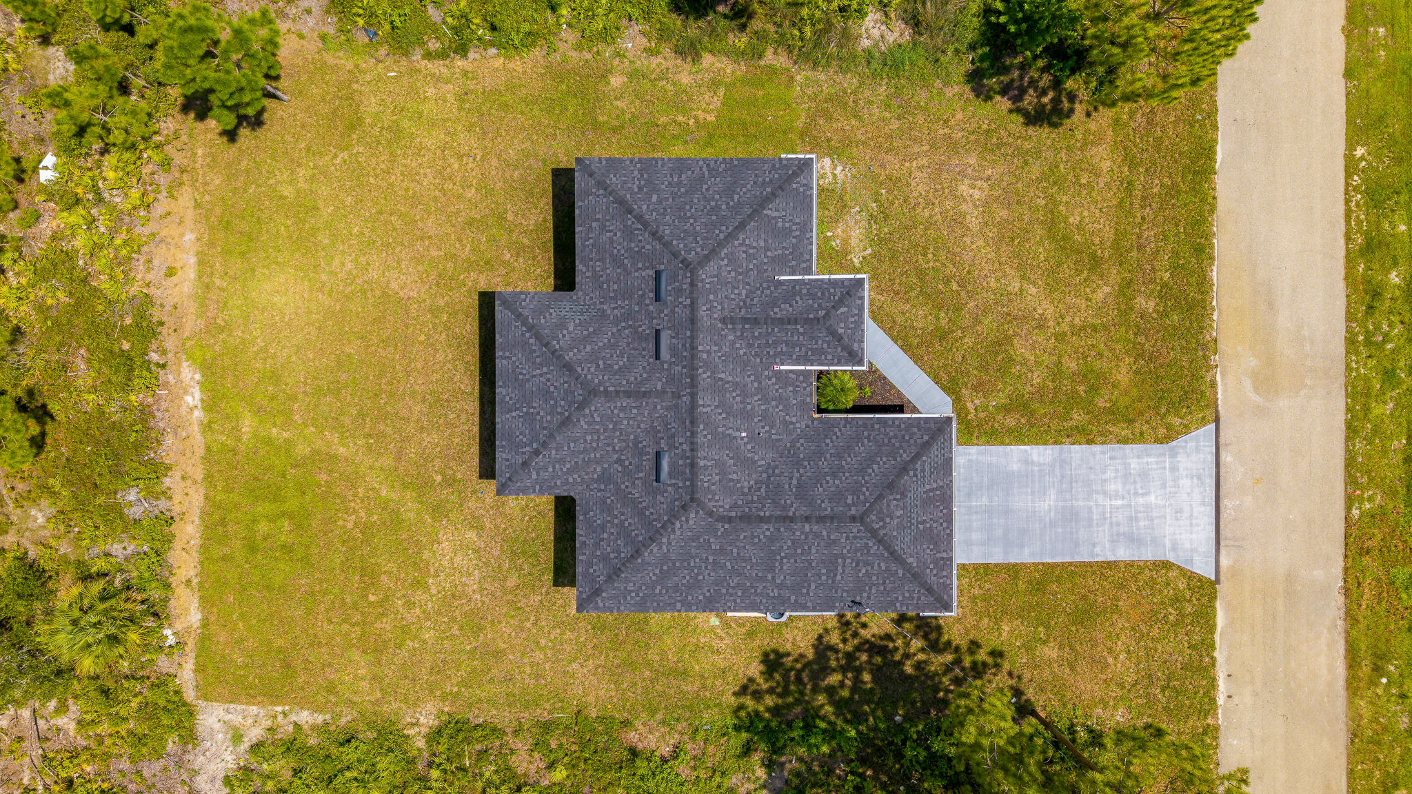 Aerial view of a Mamba Construction custom home in Lehigh Acres featuring modern architecture, dark shingle roof, and pristine landscaping