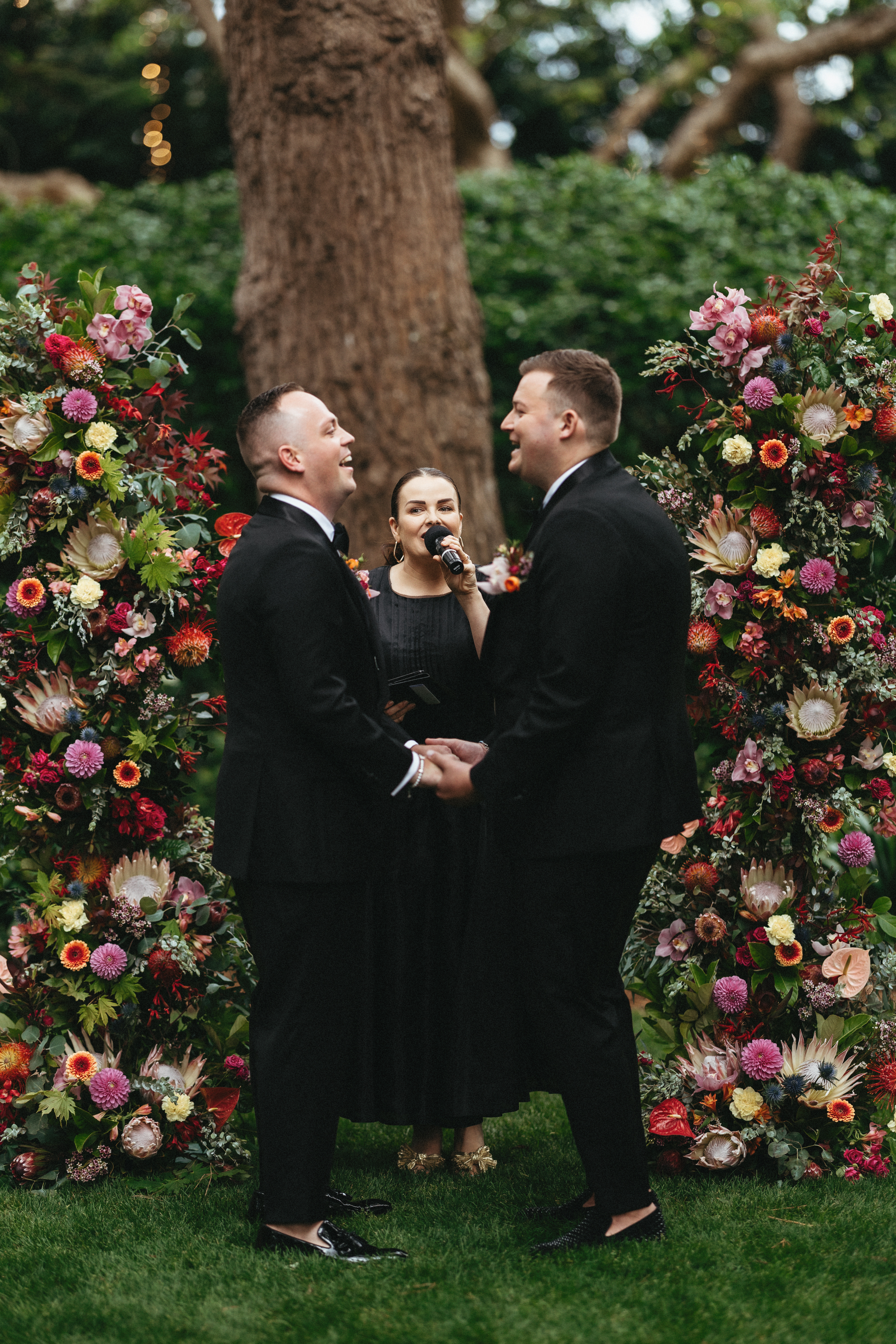 Two grooms at a floral ceremony arch