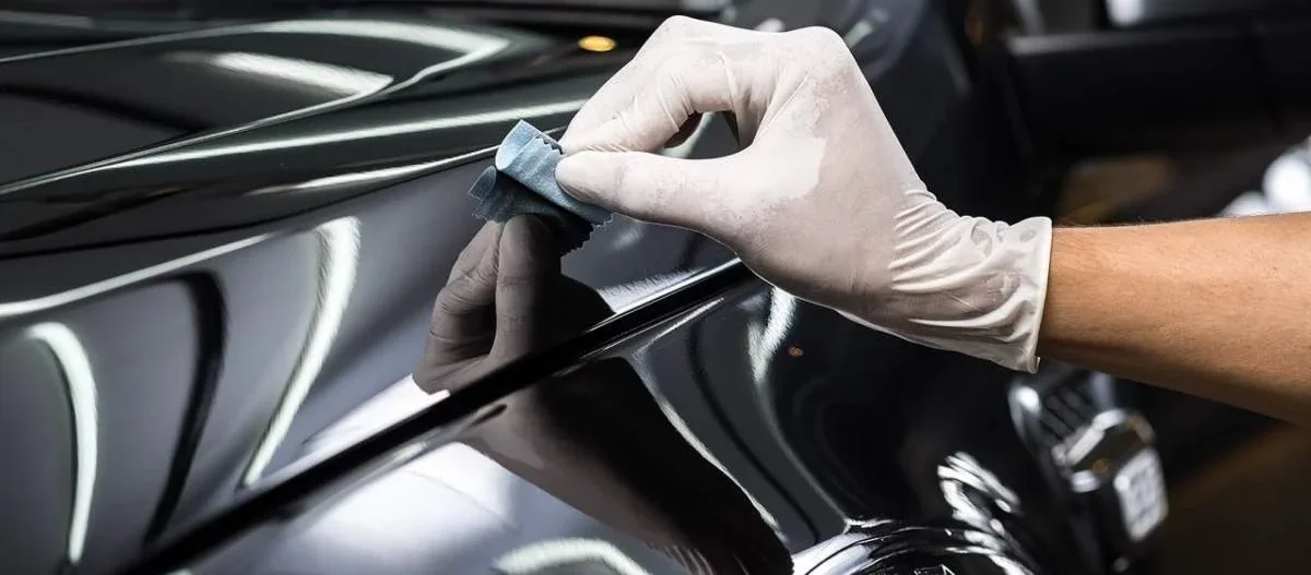 Close-up of ceramic coating being applied to a black car surface with a microfiber applicator by hand.