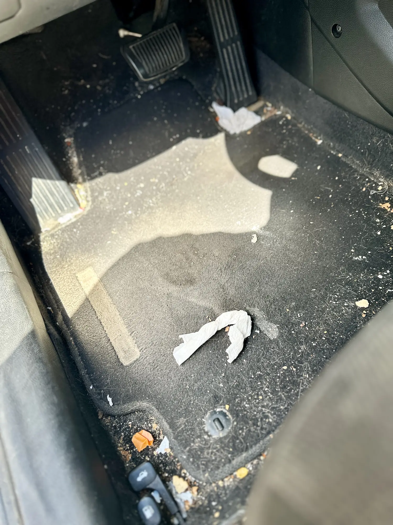 Heavily soiled driver-side floor area with trash and debris prior to vacuuming and carpet extraction.