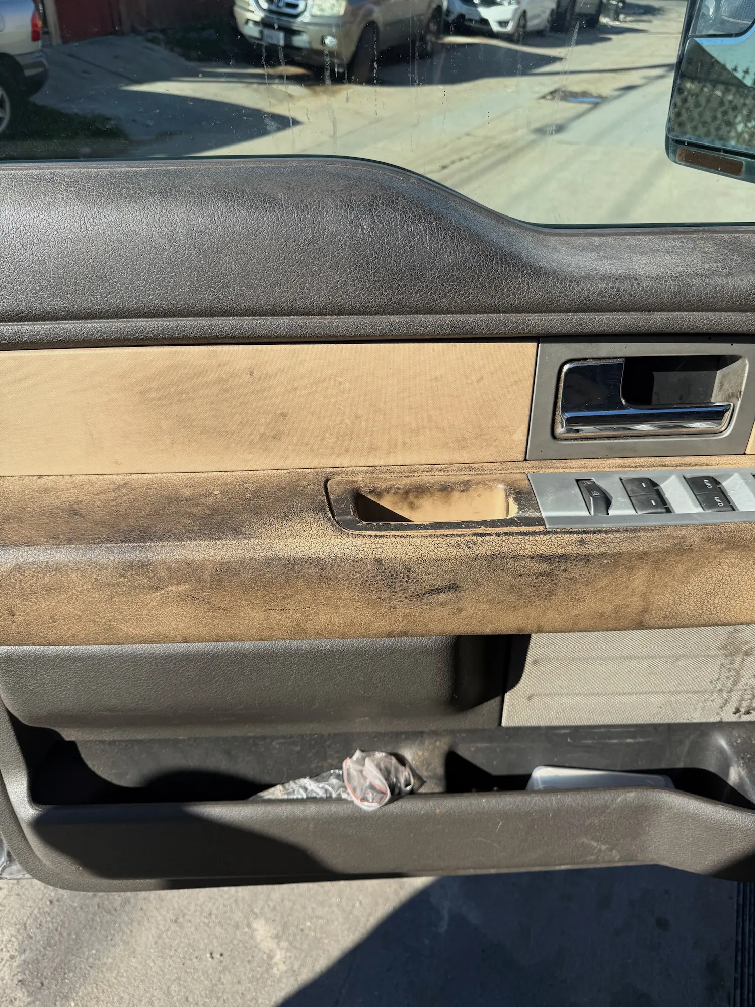  Heavily soiled tan and black car door panel with visible grime and buildup before interior detailing.
