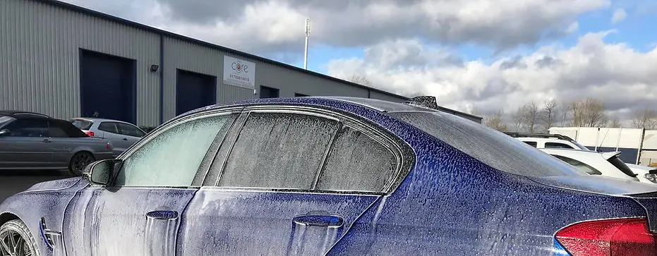 lue sedan covered in snow foam during pre-wash stage.