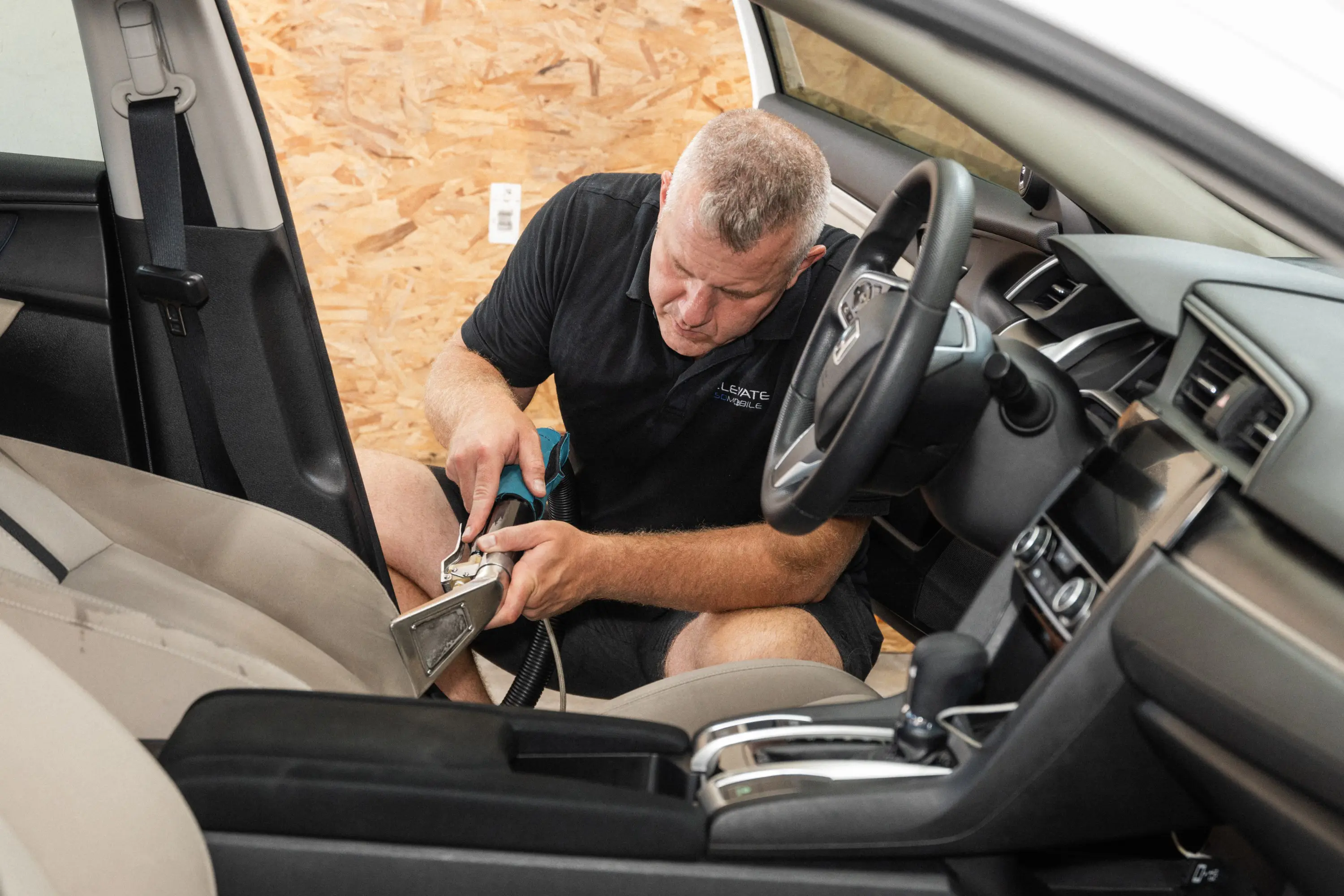 Auto detailing technician deep cleaning car seat upholstery with a hot water extractor during a full interior detailing service.