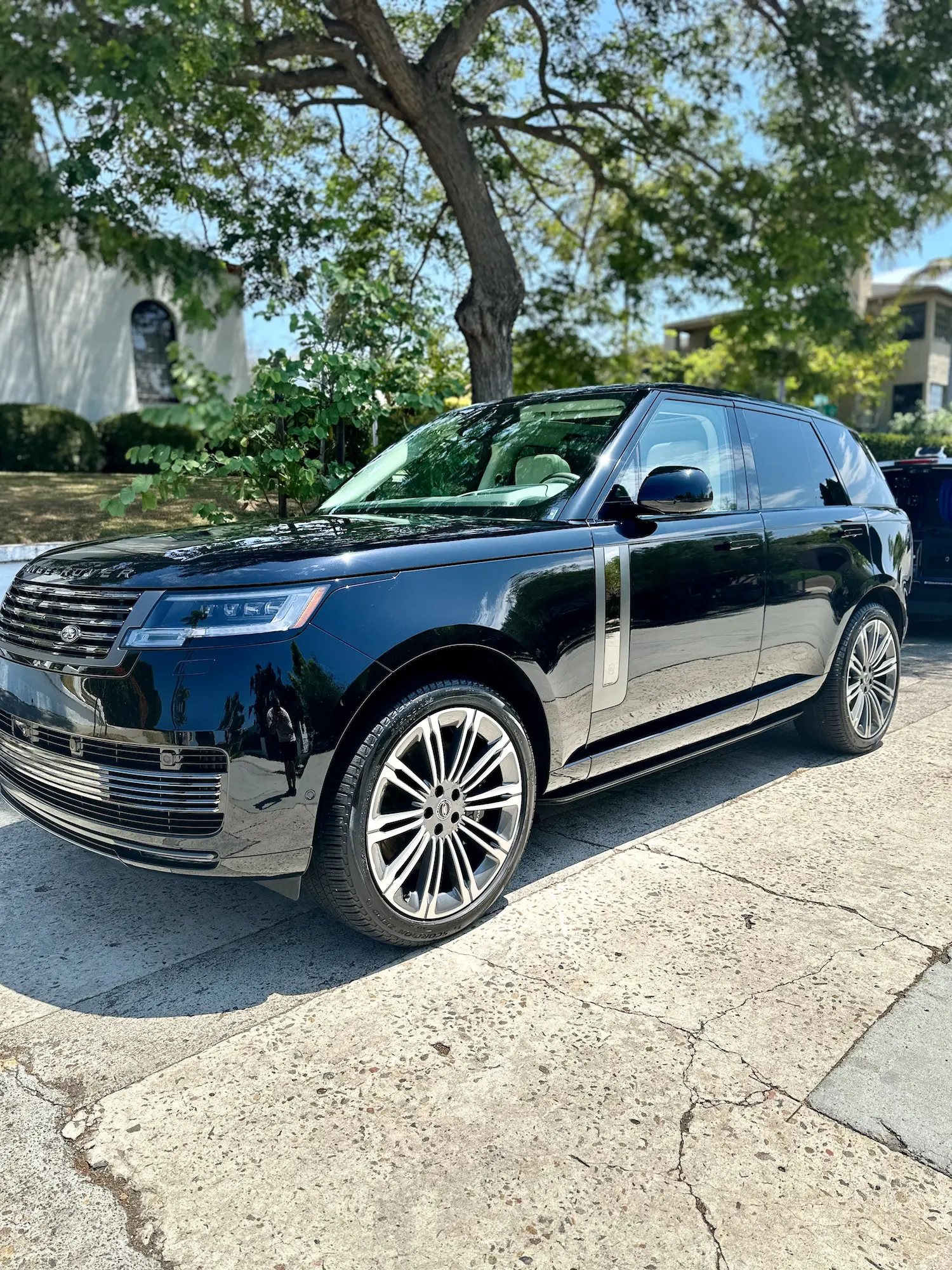 Shiny black Range Rover parked curbside on a tree-lined residential street with sun reflections on the paint.