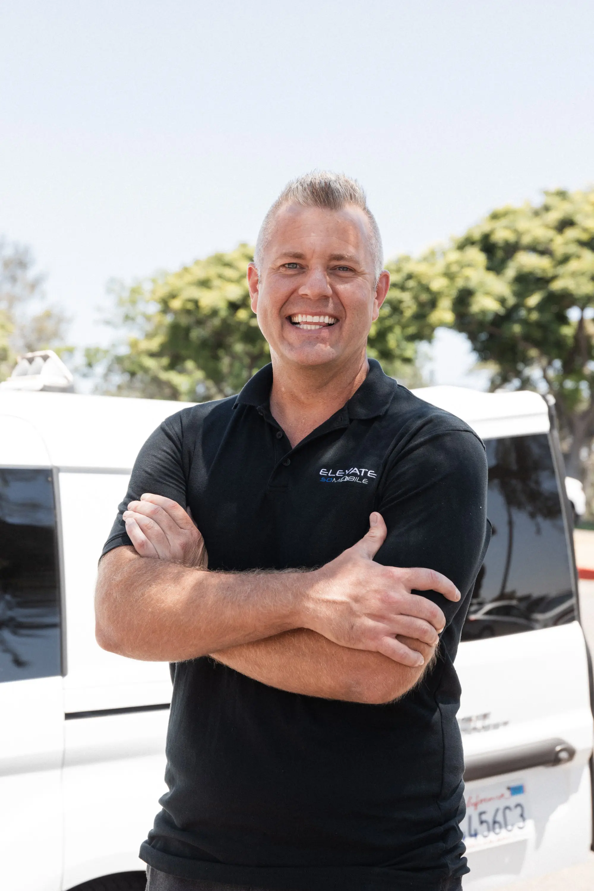 Friendly mobile auto detailing technician in branded uniform standing by detailing van, ready to serve clients.