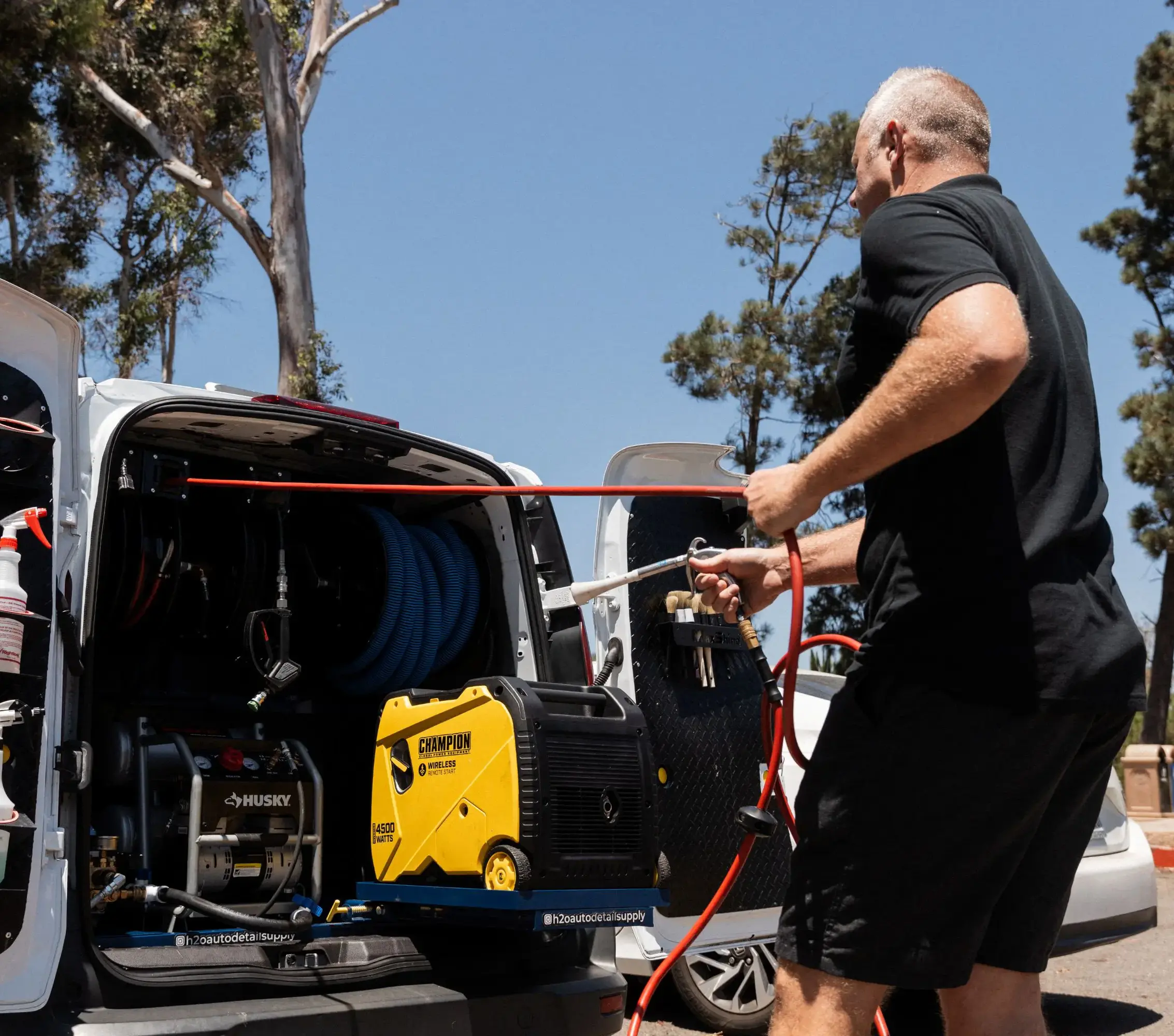 Mobile auto detailer using a power washer setup from a van equipped with professional tools.
