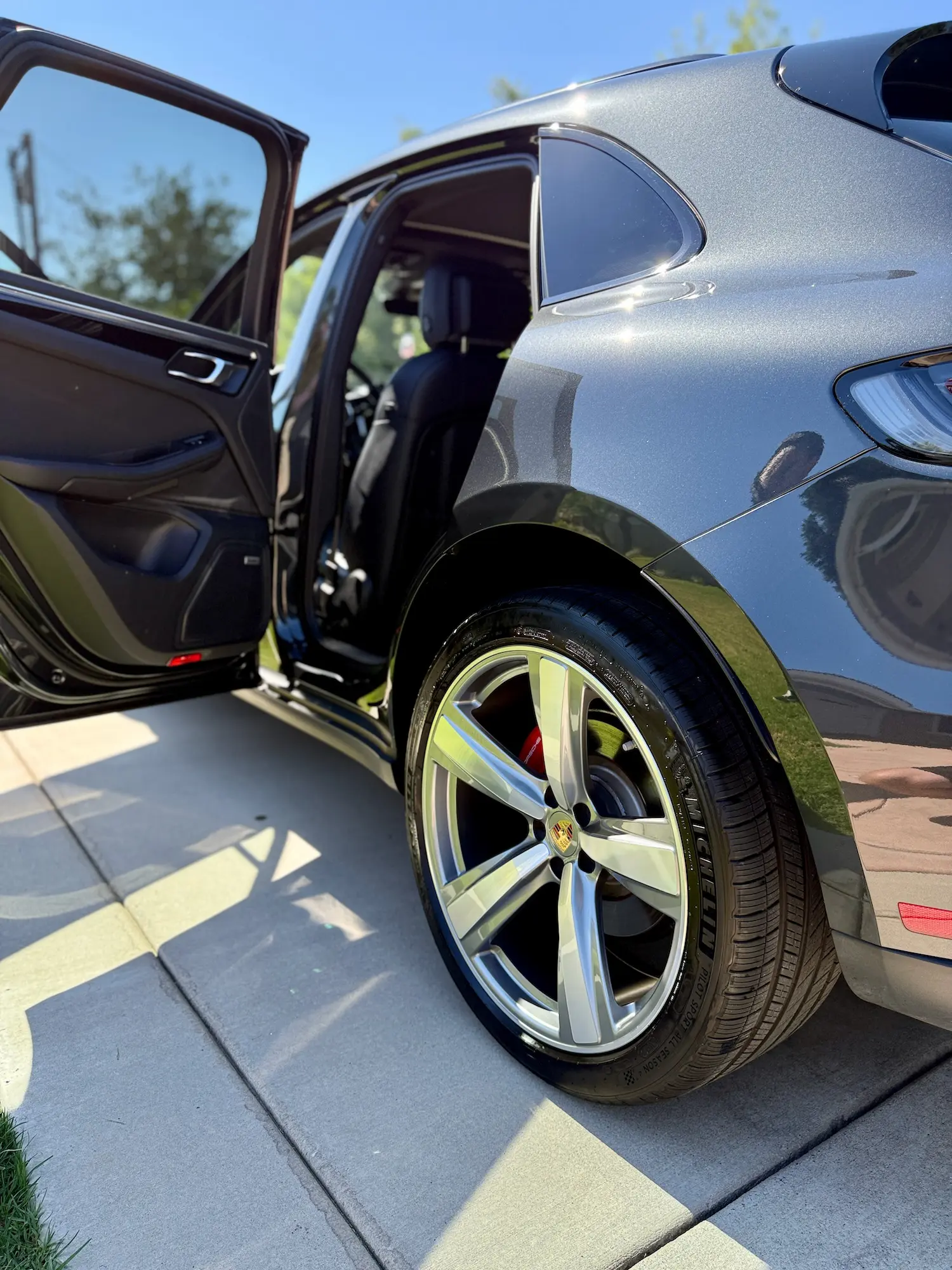 Close-up of a Porsche SUV's polished rear wheel and open passenger doors, highlighting clean detailing and reflective paint.