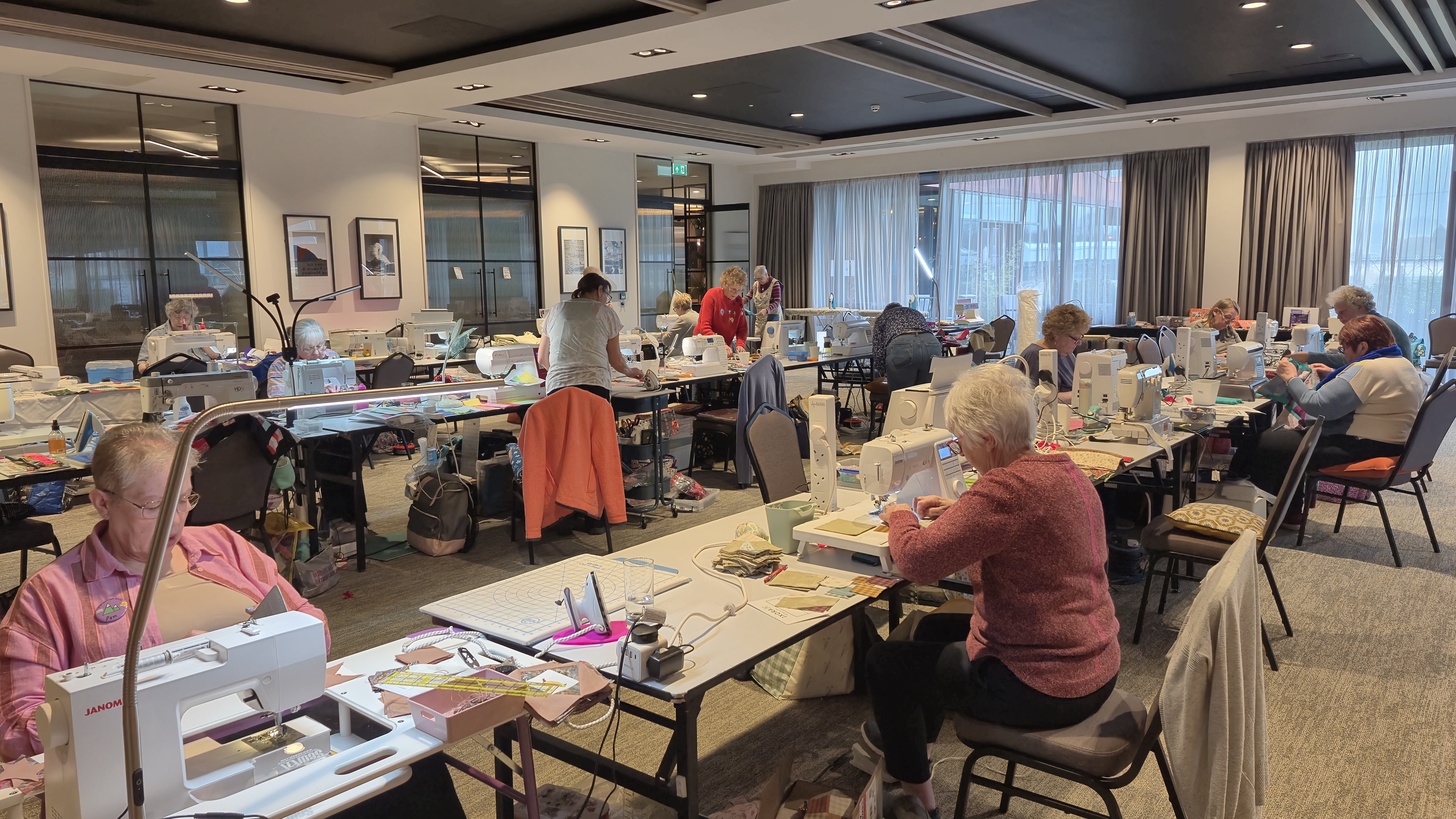 Women sewing at tables during a patchwork quilting retreat workshop surrounded by colourful fabric and sewing machines