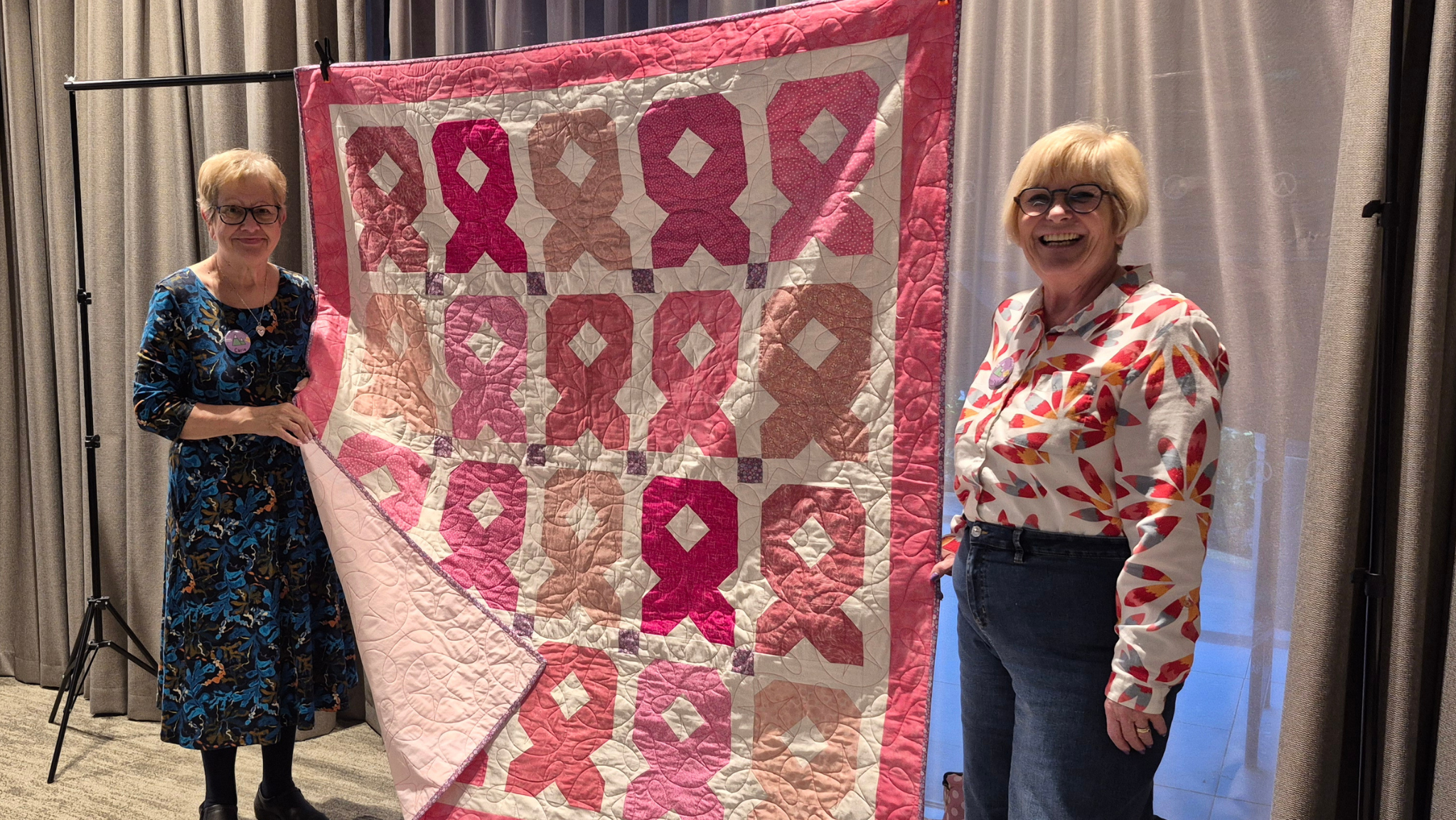 Gwenfair and Carie standing beside a pink ribbons charity quilt at the Eryri patchwork retreat in North Wales