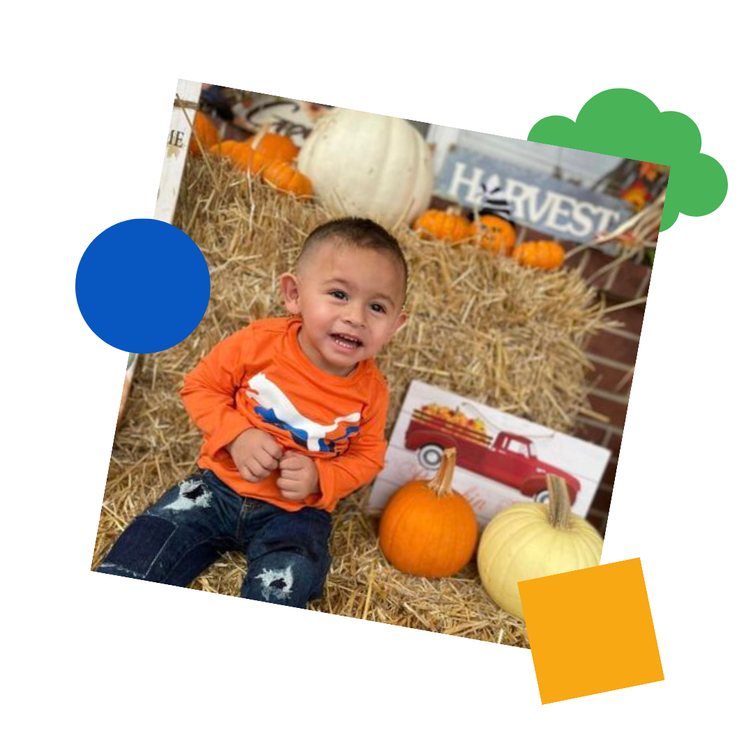 little boy sat with pumpkins on a hay stack