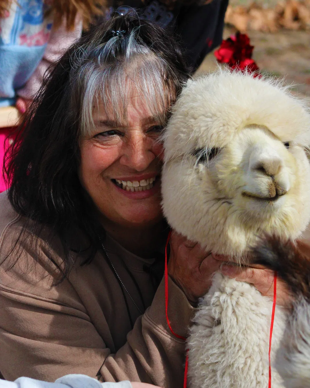 Stacey Payne, owner of Alpaca Adventures at Honey Lake, smiling and hugging one of her white Huacaya alpacas