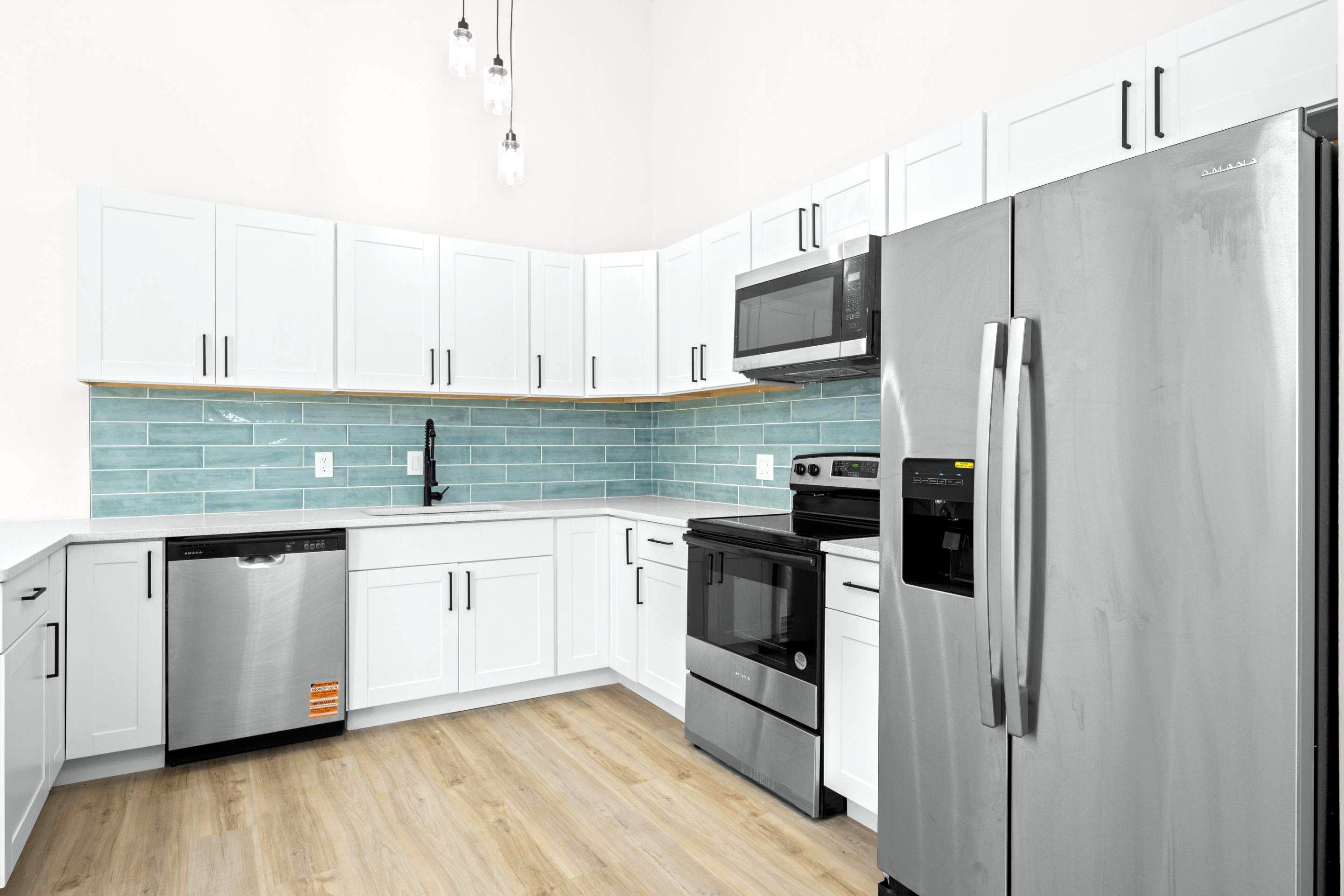 Finished white shaker kitchen with teal glass backsplash, quartz counters and stainless appliances