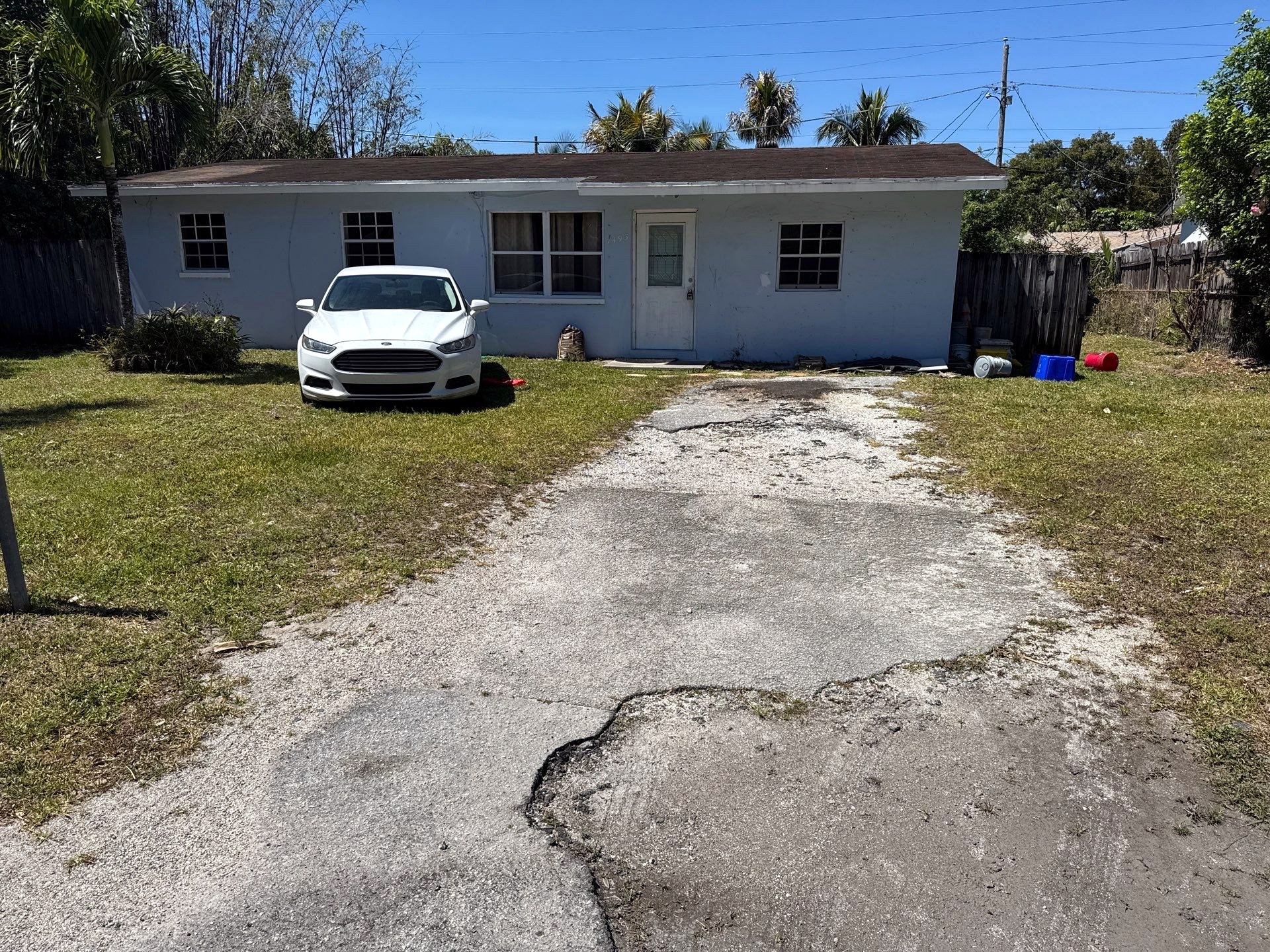 Before: worn house exterior with a cracked, patchy concrete driveway