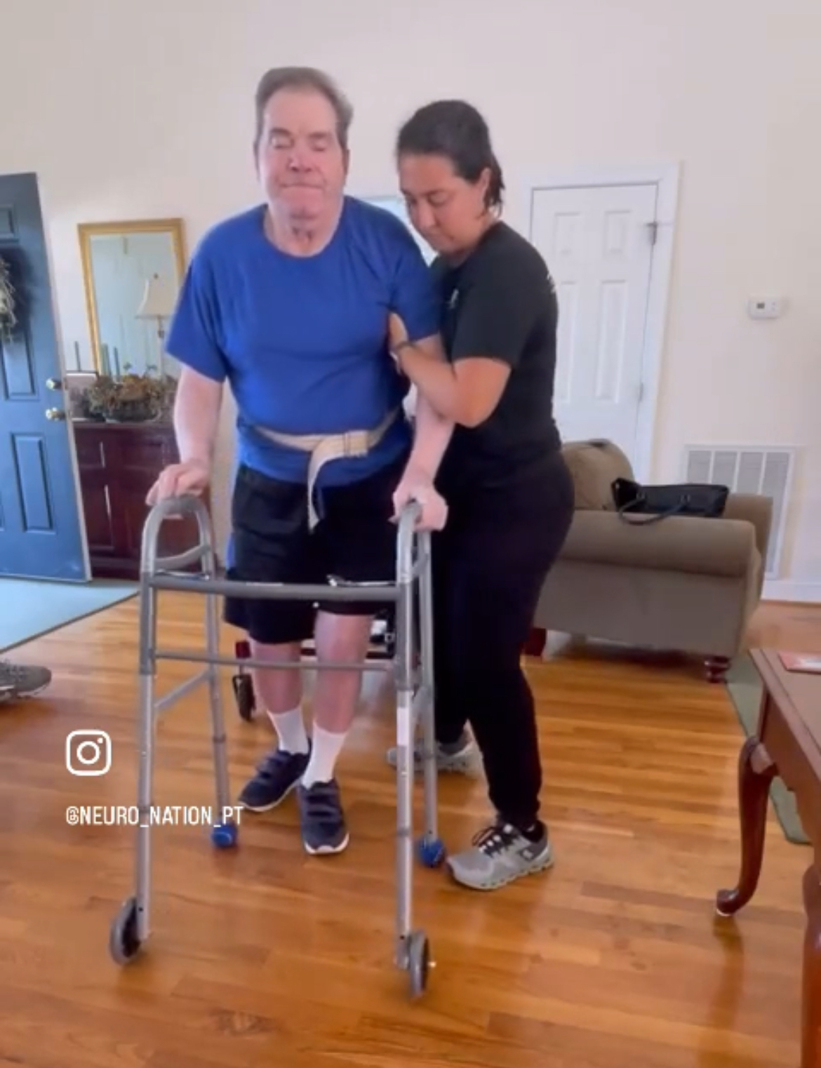 Therapist supporting a patient with a walker during in-home physical therapy.