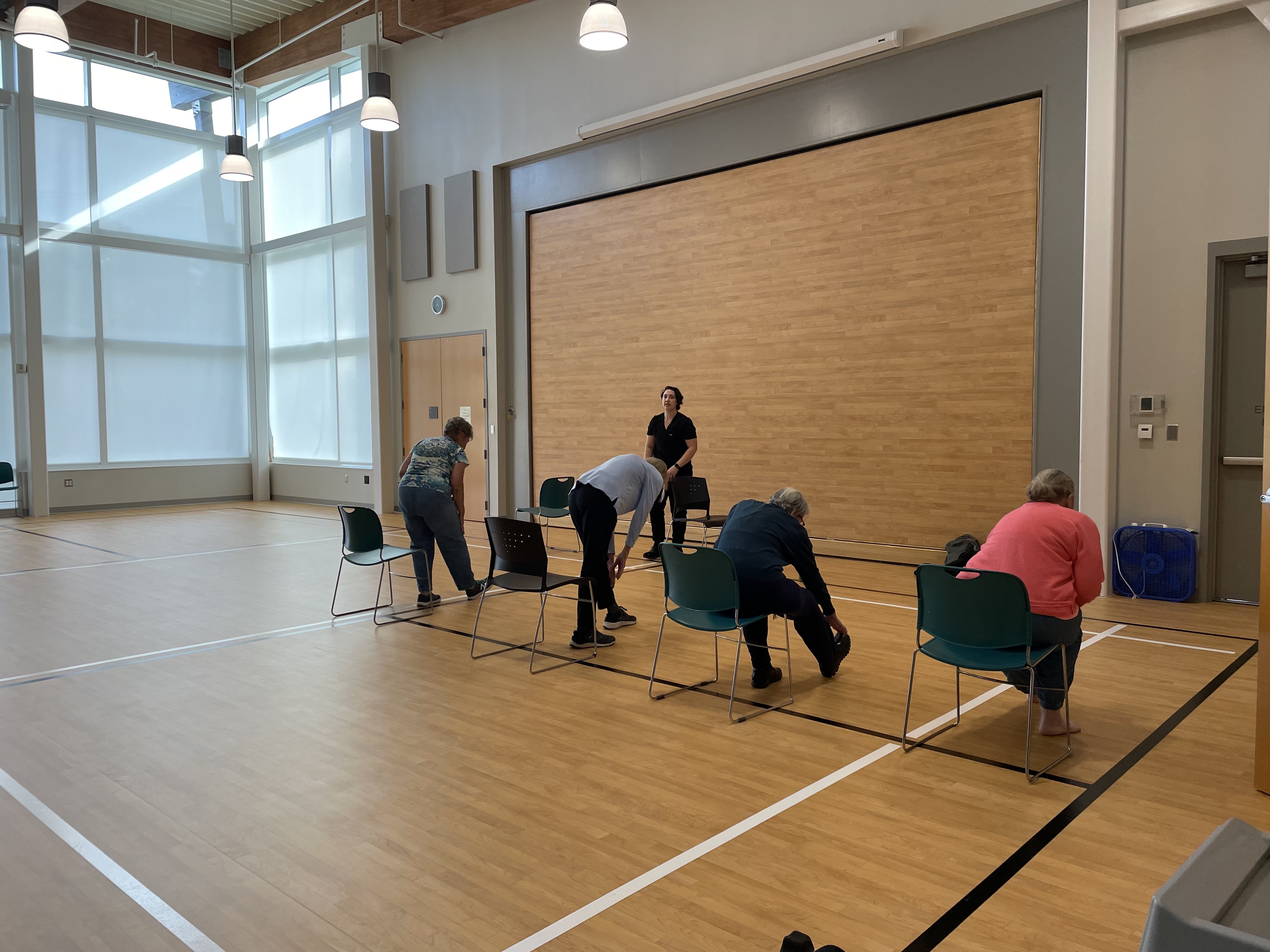 Small group fitness class doing seated and standing chair exercises led by an instructor in a studio.