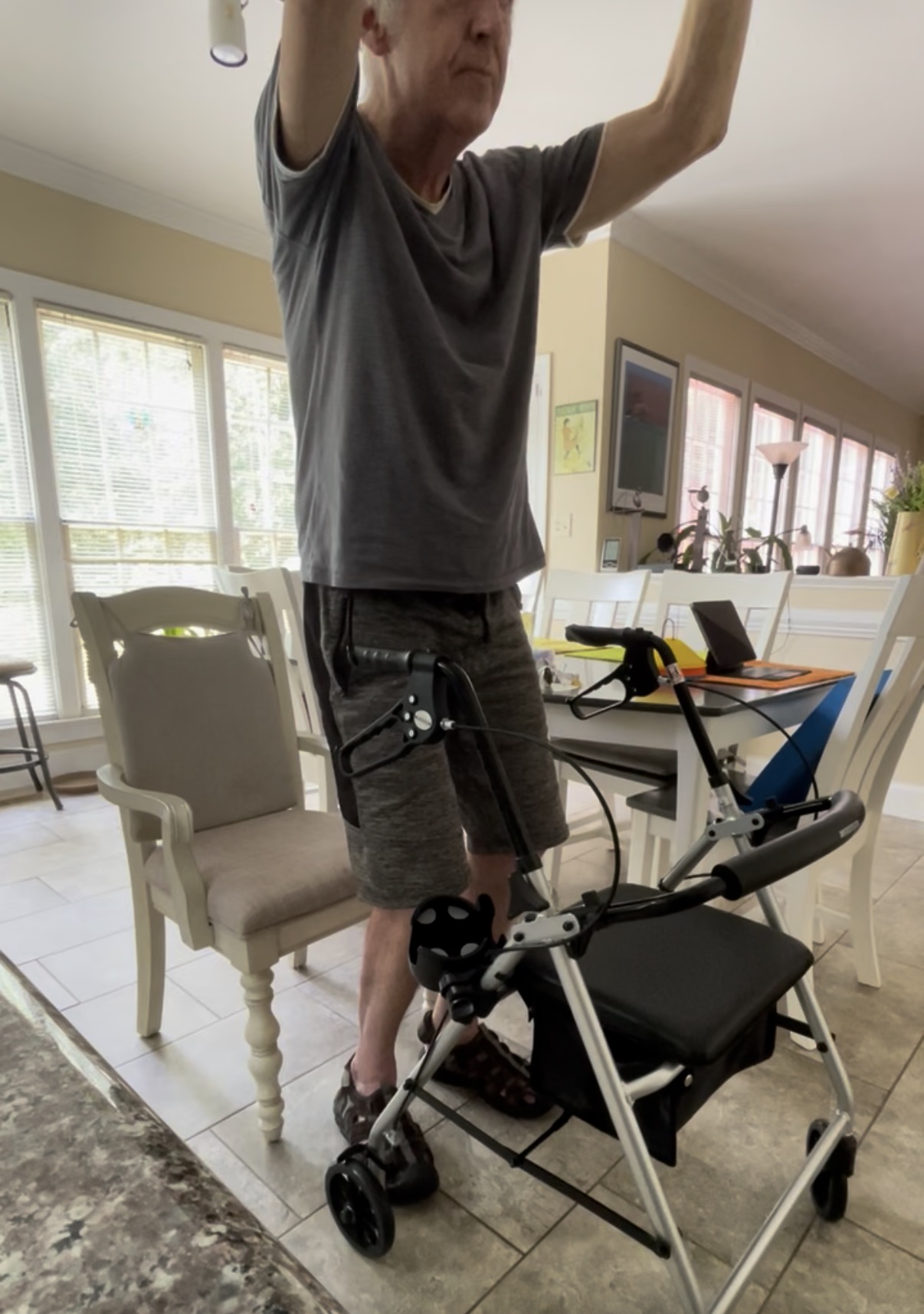 Patient standing and doing an overhead reaching exercise with his rollator walker during in-home physical therapy.