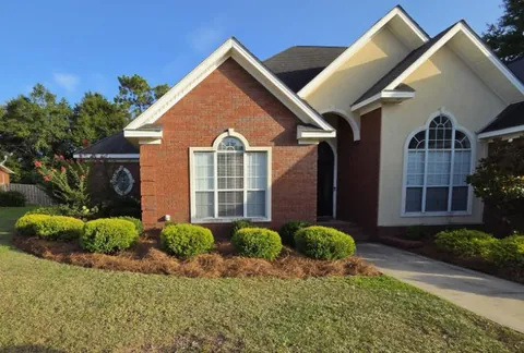 Curved pine straw mulch bed with rounded green shrubs and a freshly mowed lawn in front of a red brick and cream stucco home