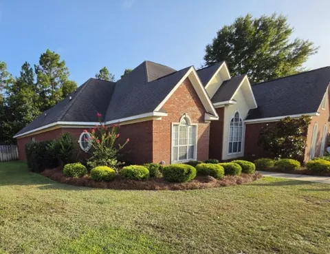 Mowed lawn with a wide pine straw mulch bed and rounded shrubs in front of a red brick home with a gabled roof