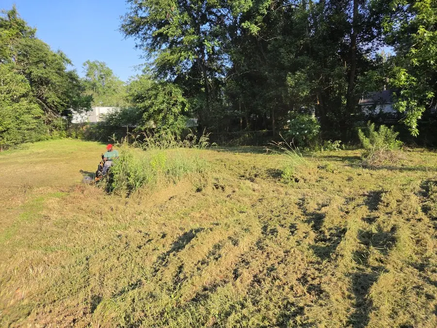 Person on a zero-turn mower cutting a large overgrown lot with tall grass