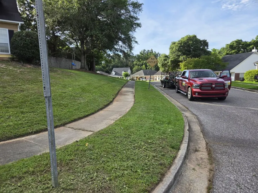 Red work truck and black trailer loaded with mowers and trimmers parked on a residential street in Mobile, Alabama