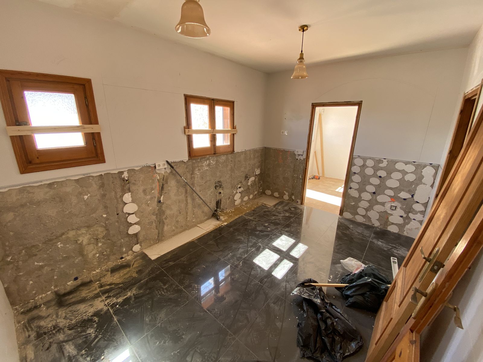 A kitchen Leon has stripped out, old wall tiles hacked off above a black tiled floor