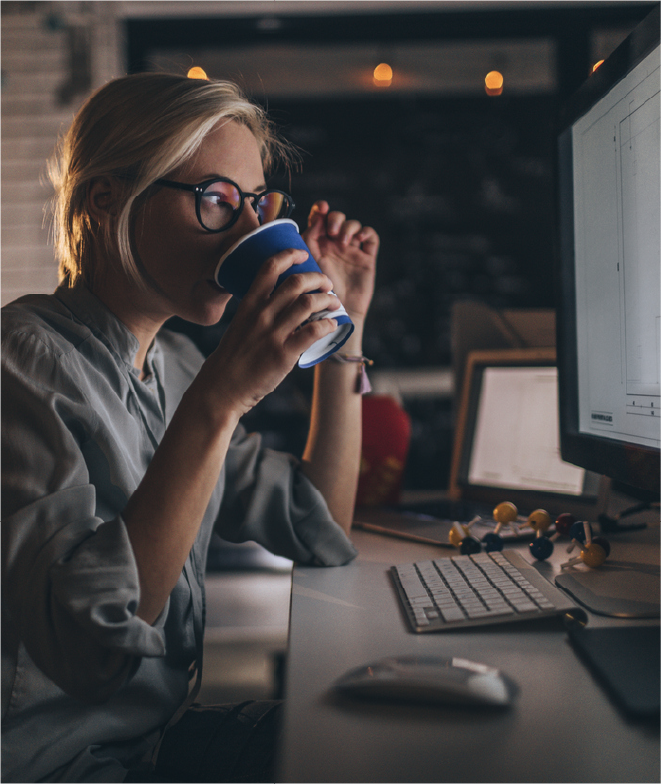 Designer working late at a computer while drinking from a cup.