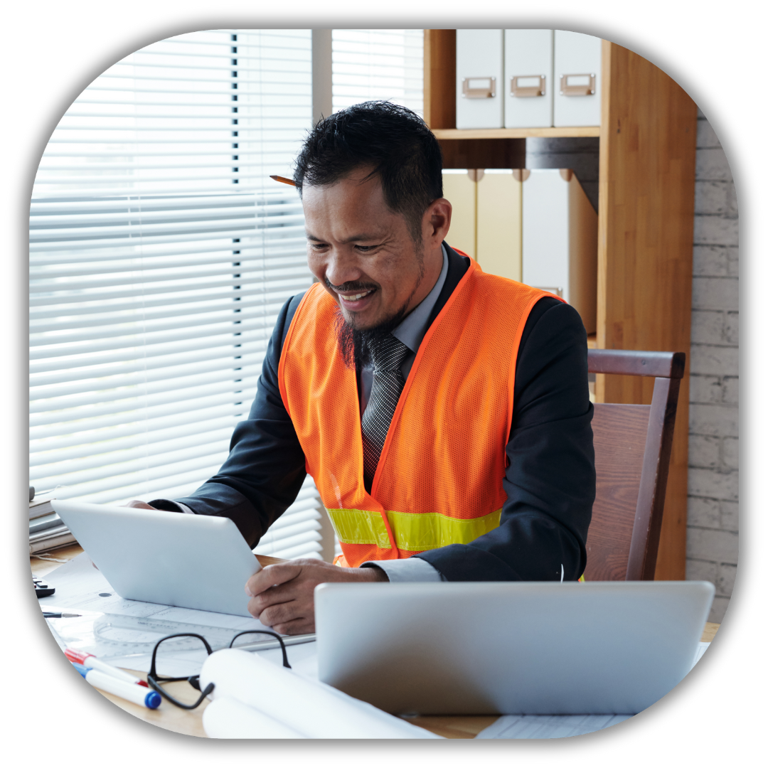 Smiling contractor in a suit and safety vest working on a tablet in an office setting, representing financial planning and profit optimization for residential contractors to ensure predictable cash flow and profitability.