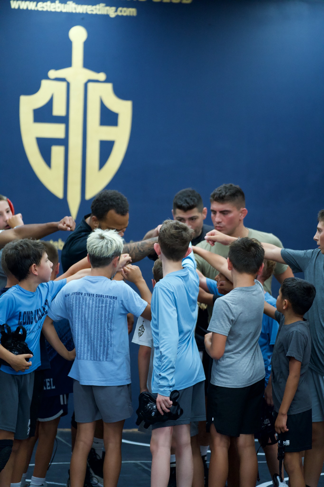 Youth wrestlers in a team huddle with the Este Built crest at Este Built Wrestling Club