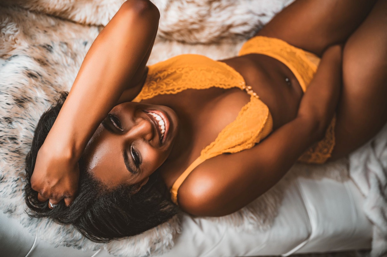 Smiling woman in yellow lace lingerie lying on soft blanket, intimate close-up boudoir portrait with warm tones