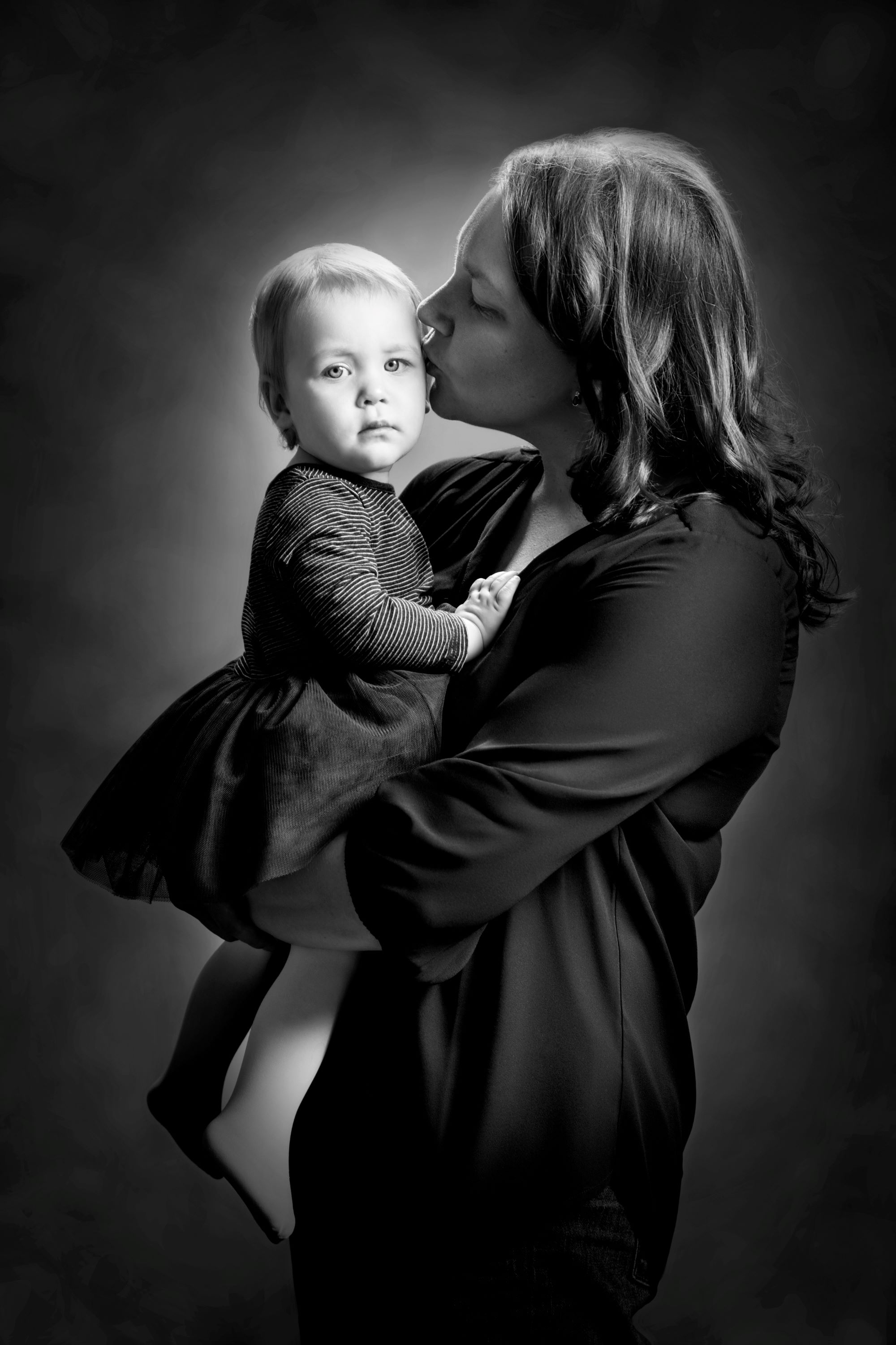 Black and white studio portrait of a mother kissing her daughter's face