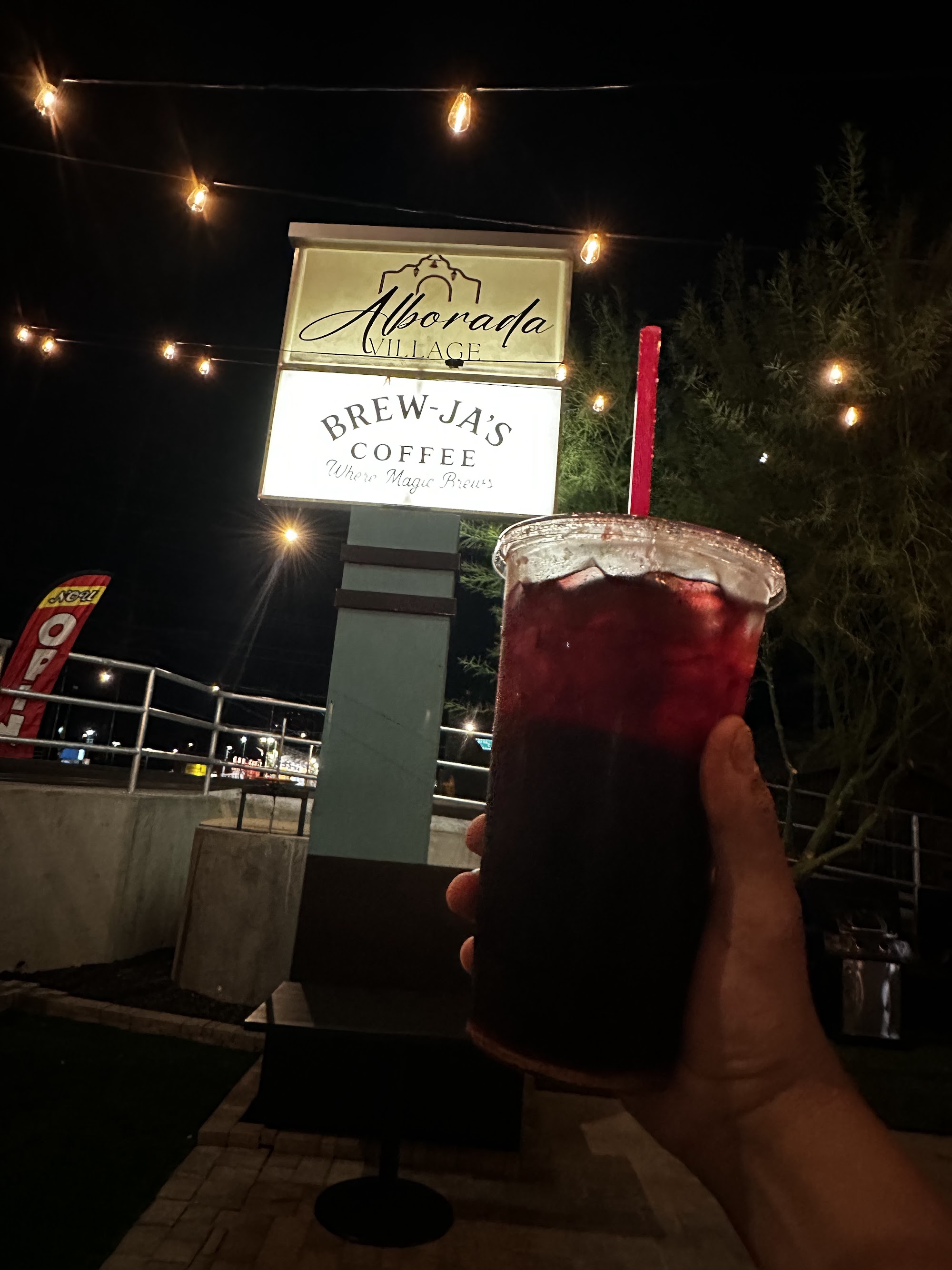 Deep red berry iced drink held in front of lit Alborada and Brew-Ja's pylon sign at night